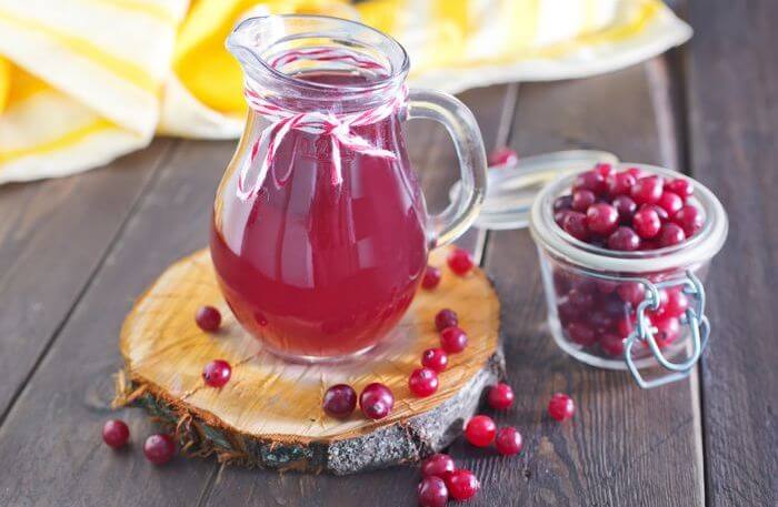 Cranberry juice in a jar with cranberries lying around it.