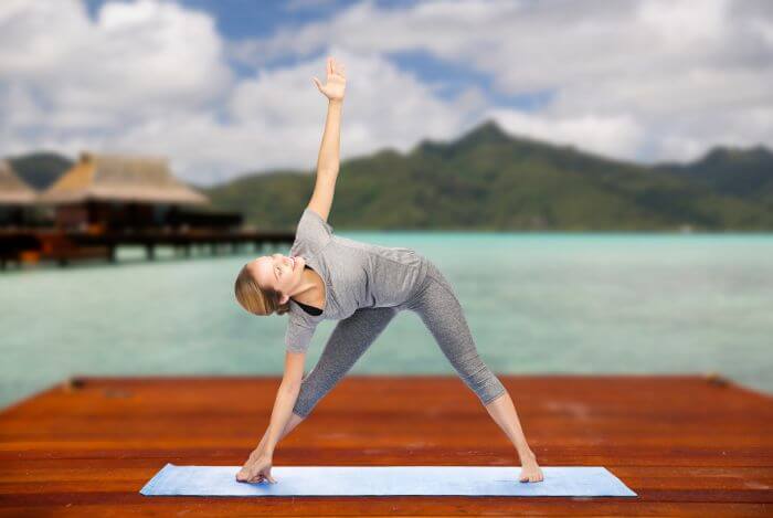 Woman in Triangle Pose (Trikonasan). Scenic Background with Lake and Mountain in Backdrop.