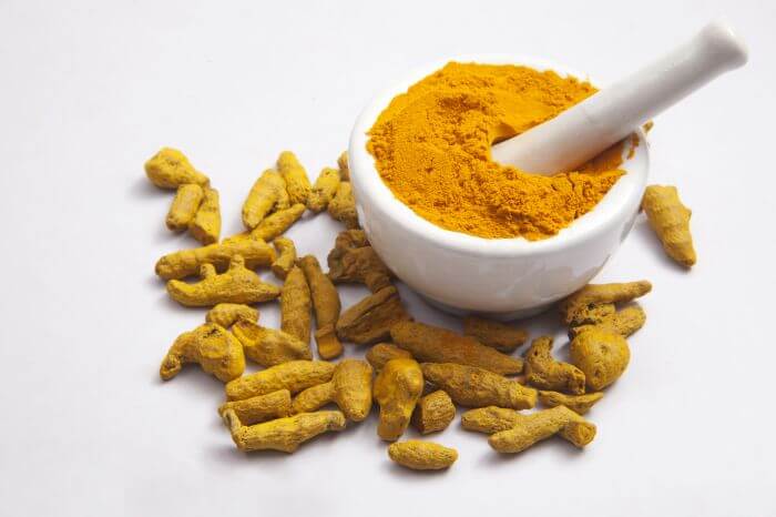 Turmeric powder in mortar with Turmeric roots isolated on white background