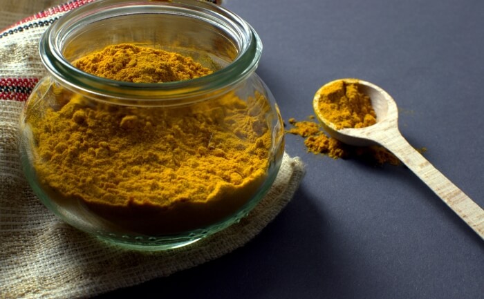 Haldi in a bowl. Bowl half filled with turmeric powder with a wooden spoon lying on right side.