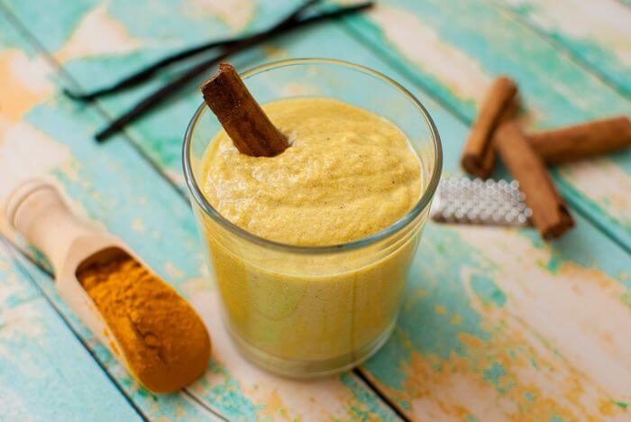 Yellow color turmeric smoothie in a glass with cinnamon sticks on the side.